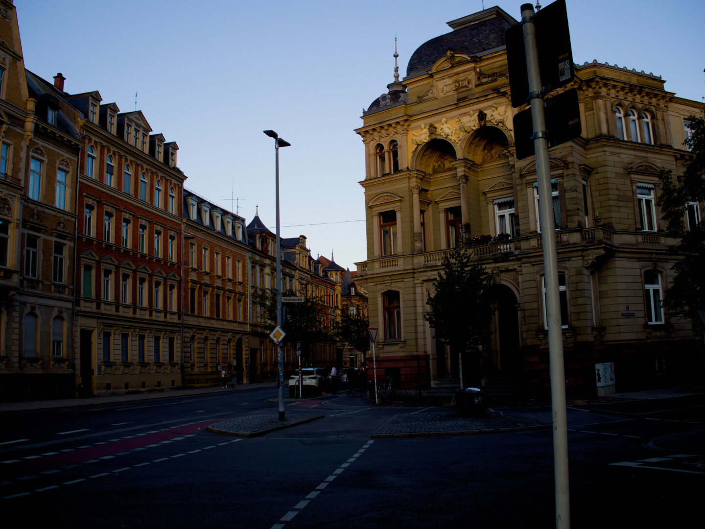 Rechts altes Sandsteinhaus. Links weitere Häuser und Straße Abendstimmung. Von der Sonne angestrahlt.