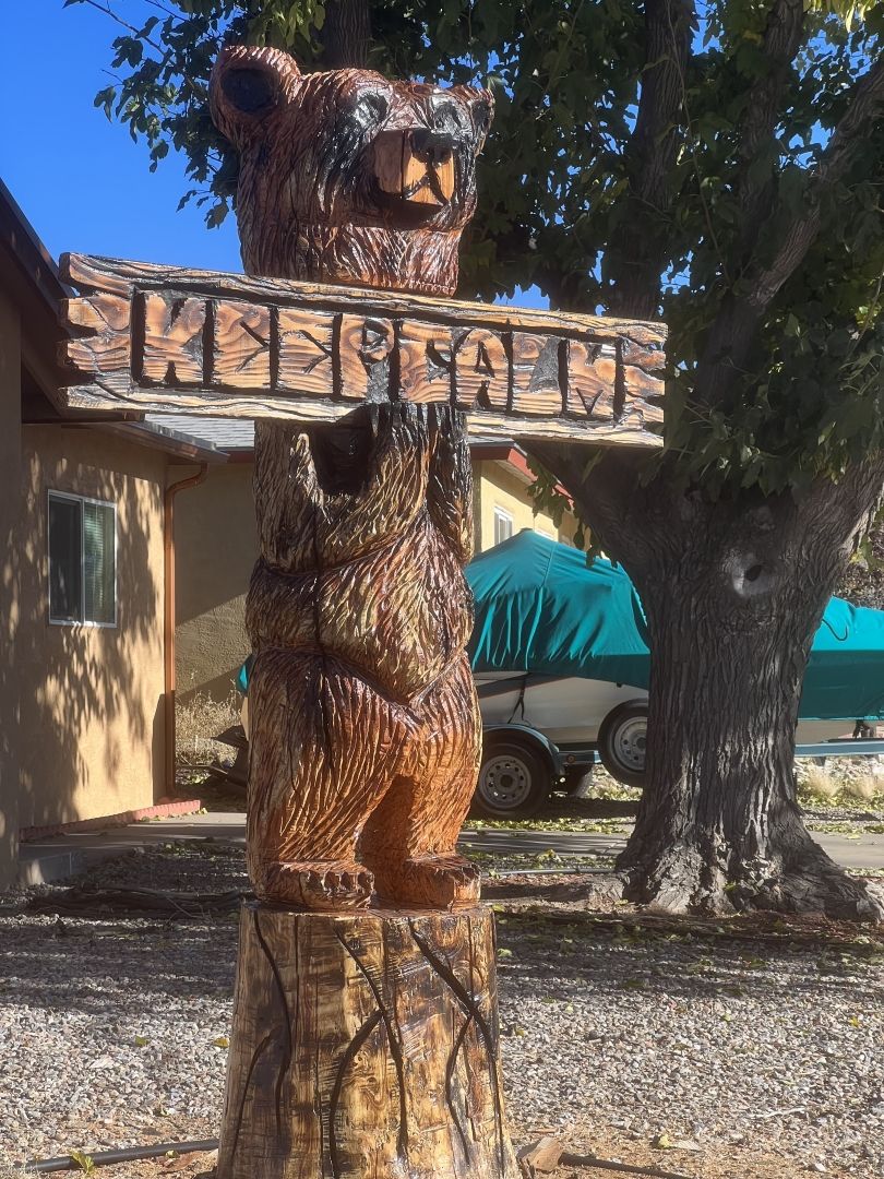 Wooden bear statue standing on a stump, holding a sign that says 'Keep calm'