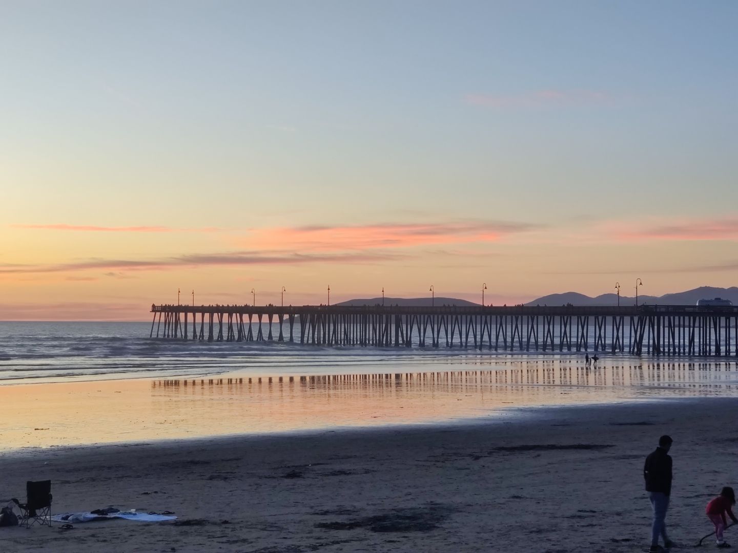 Pismo Beach pier at sunset at low tide. The sand is exceptionally reflective and the pylons of the pier shimmering reflection is mesmerizing.