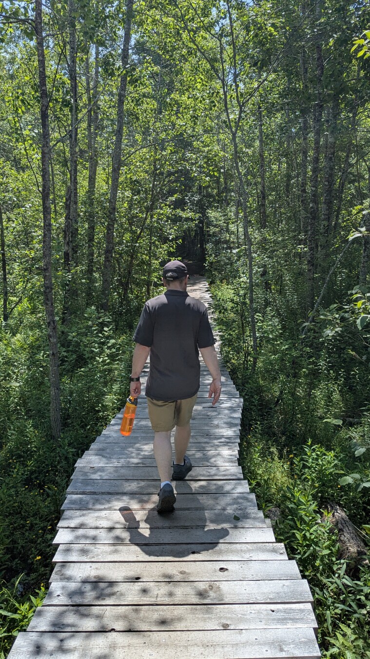 Middle aged white guy walking away on a boardwalk in the forest