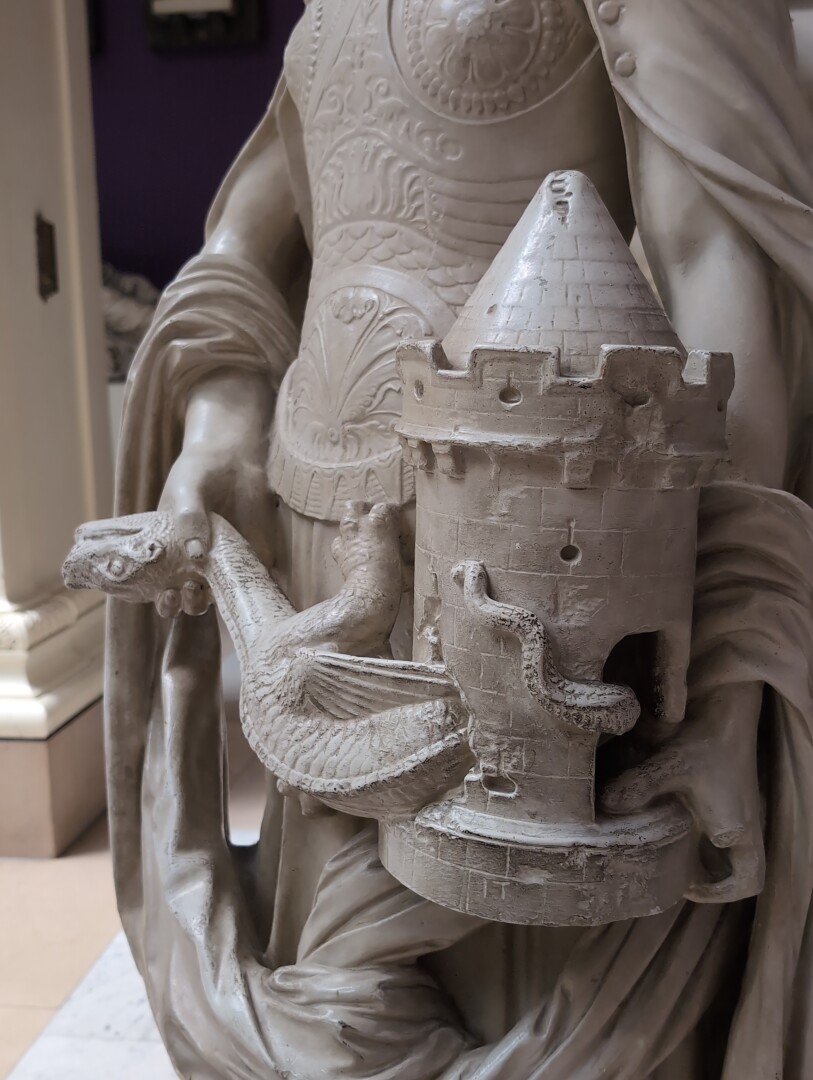 Stone carving of a woman subduing a monstrous serpent threaded through a tower turret