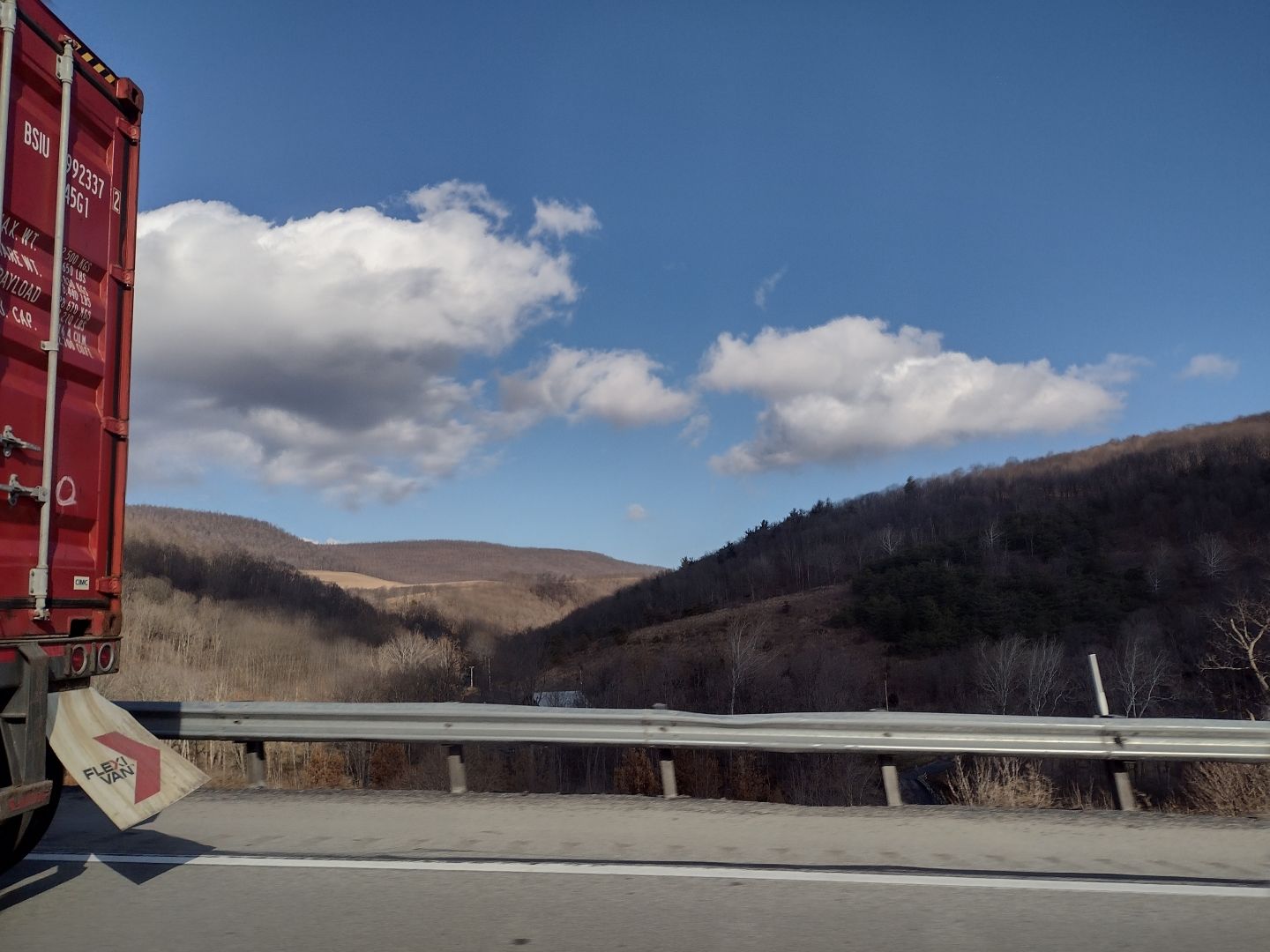 The back of a red shipping container truck driving down a wintry highway with rolling hills in the background.
