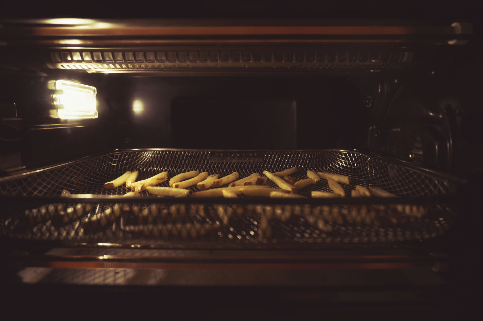 A view into an air frier frying potatoes.