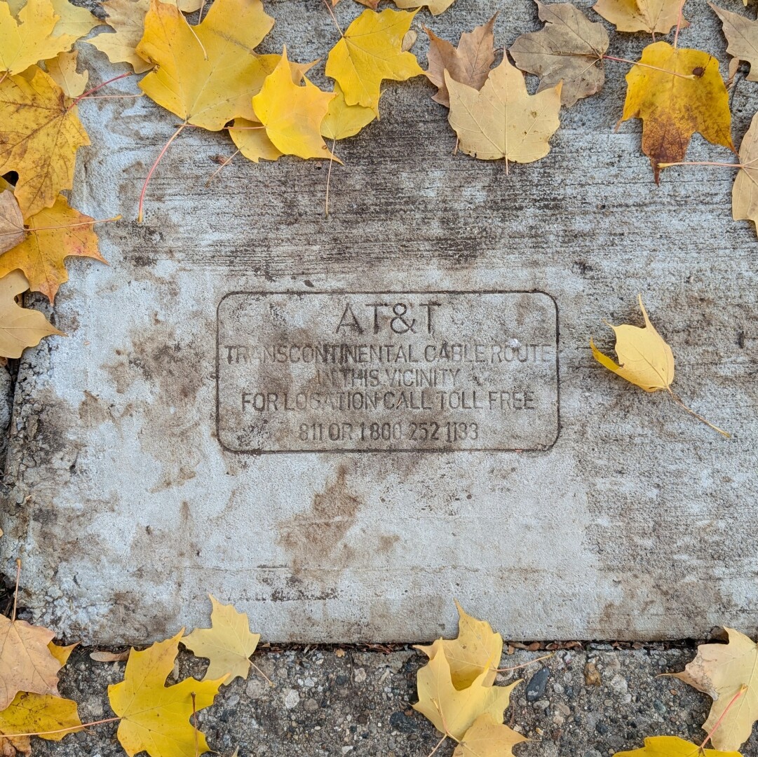 A stamp in concrete sidewalk stating "AT&T transcontinental cable route in this vicinity. For location call toll-free "