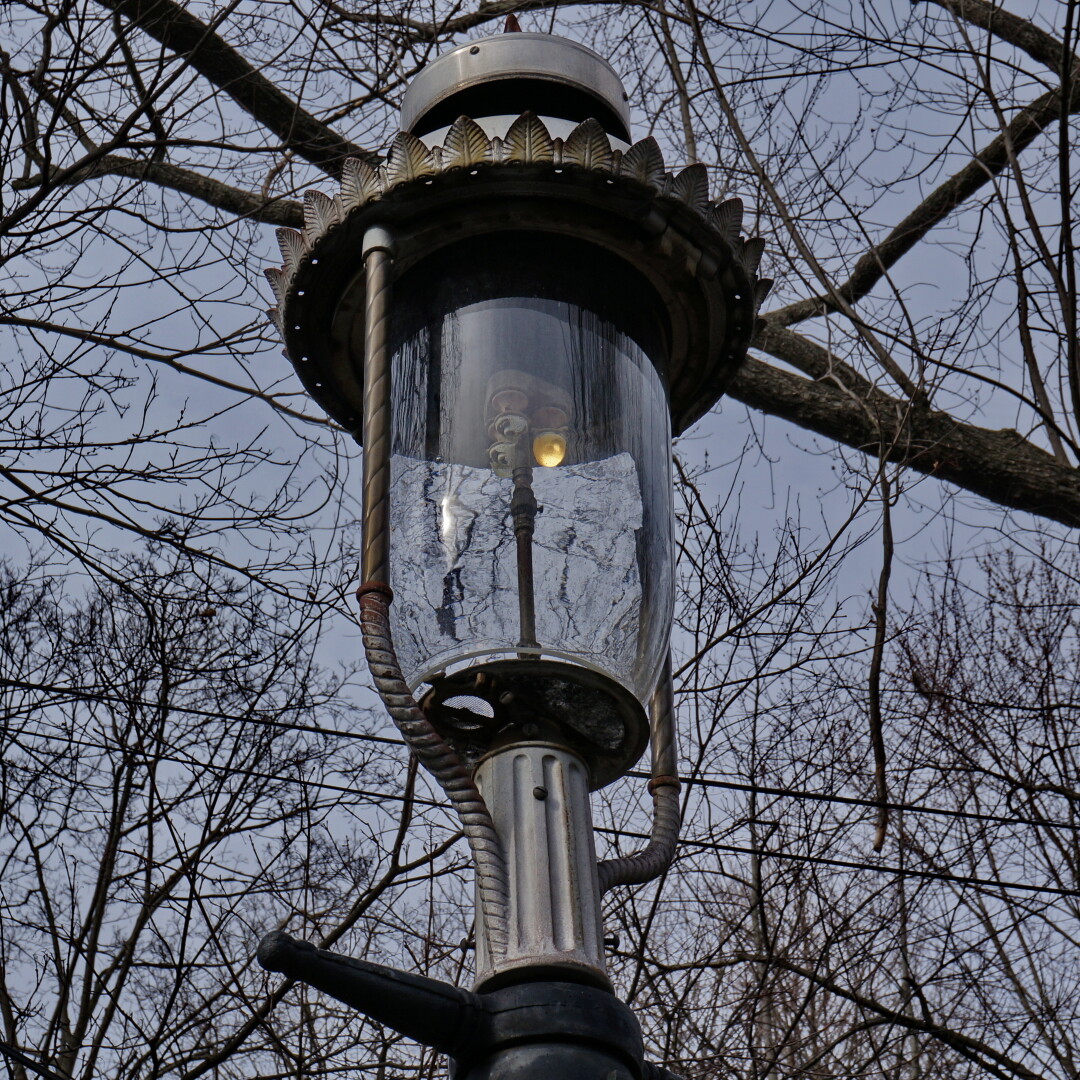 A photo of a lit gas lamp in Jamaica Plain, MA with three mantles, with only one actually producing the light.