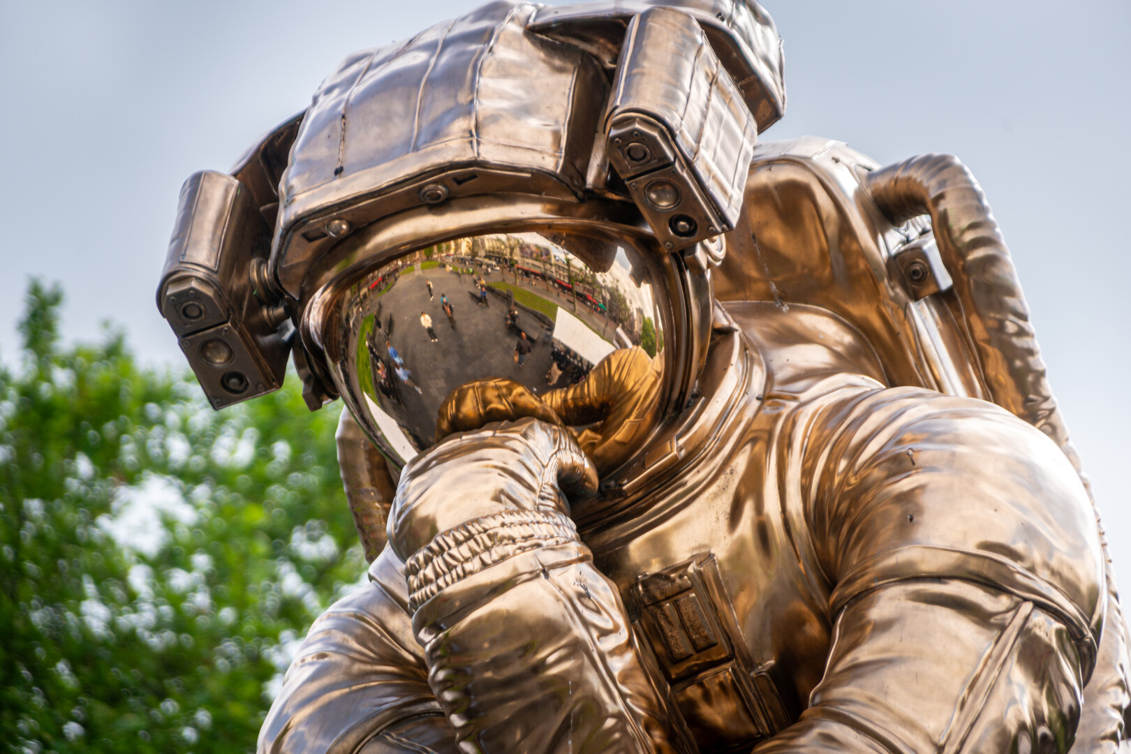 Statue of a 'golden' coloured astronaut. He sits in the same pose as the "Le Penseur" statue of Rodin: the head/helmet rests on his hand.