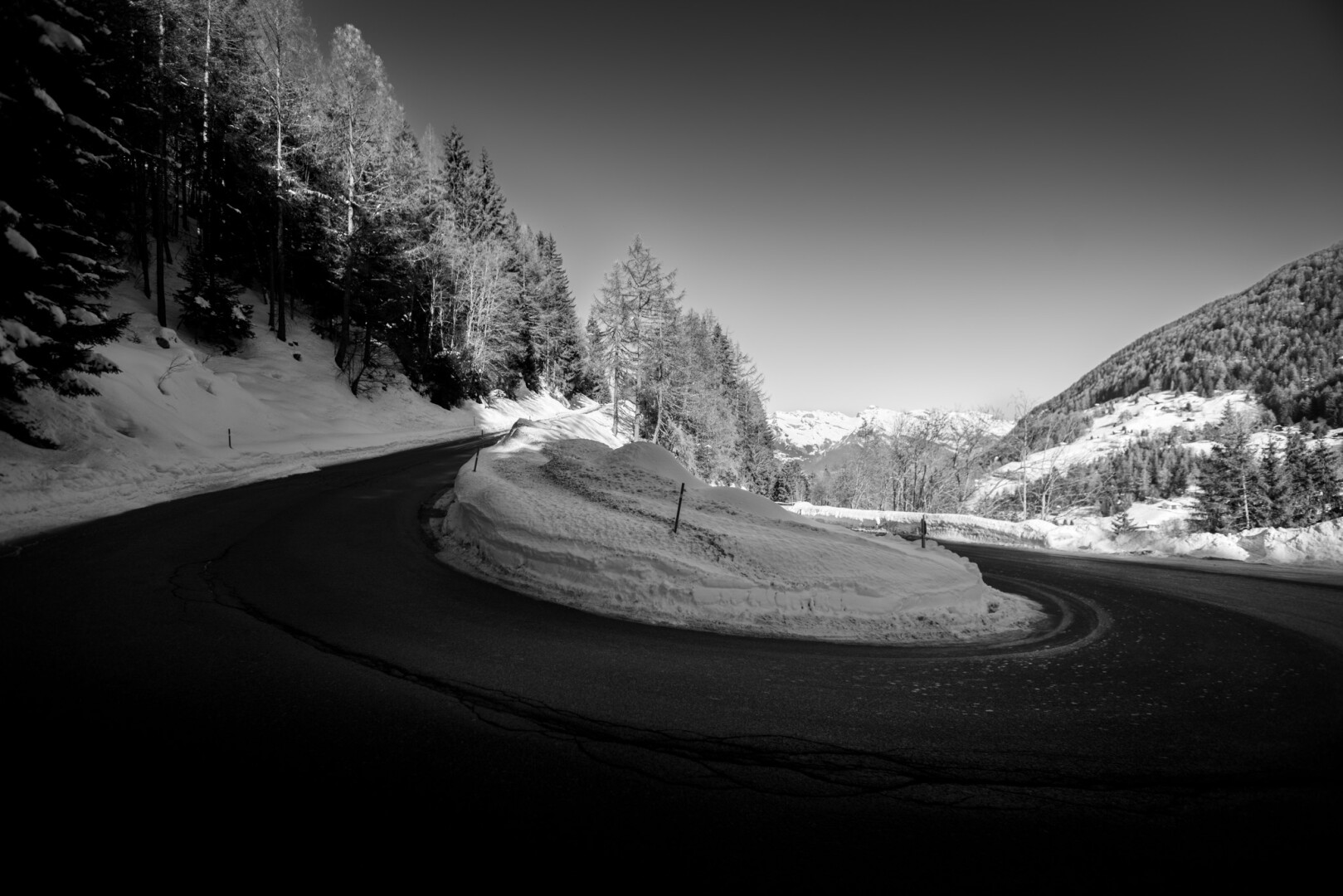 Corner of a mountain road. Black and white. The snow covers the sides of the road.