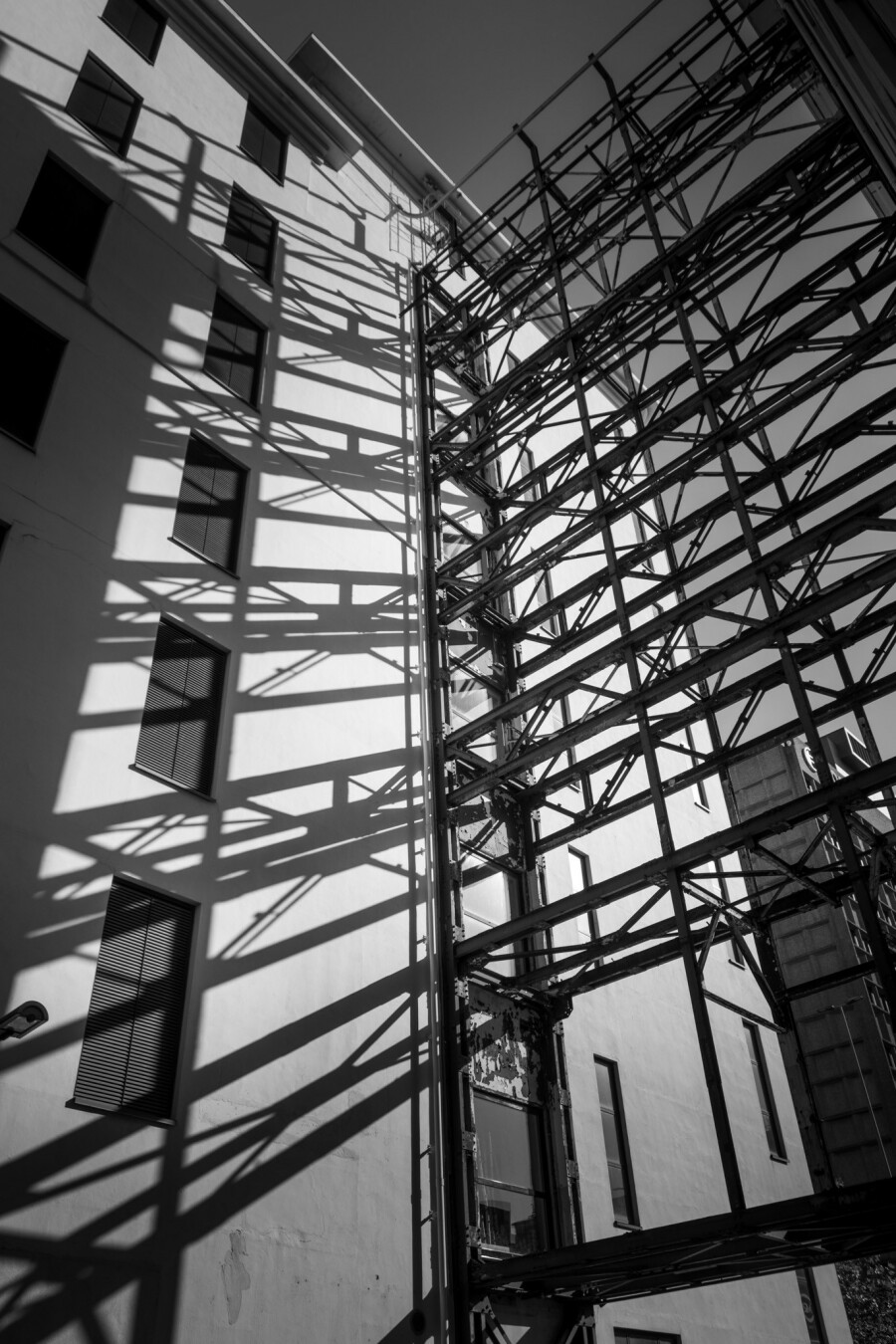 Black and white picture. Old factory wall in sunlight. The shadow of metal bars are visible on the white wall.