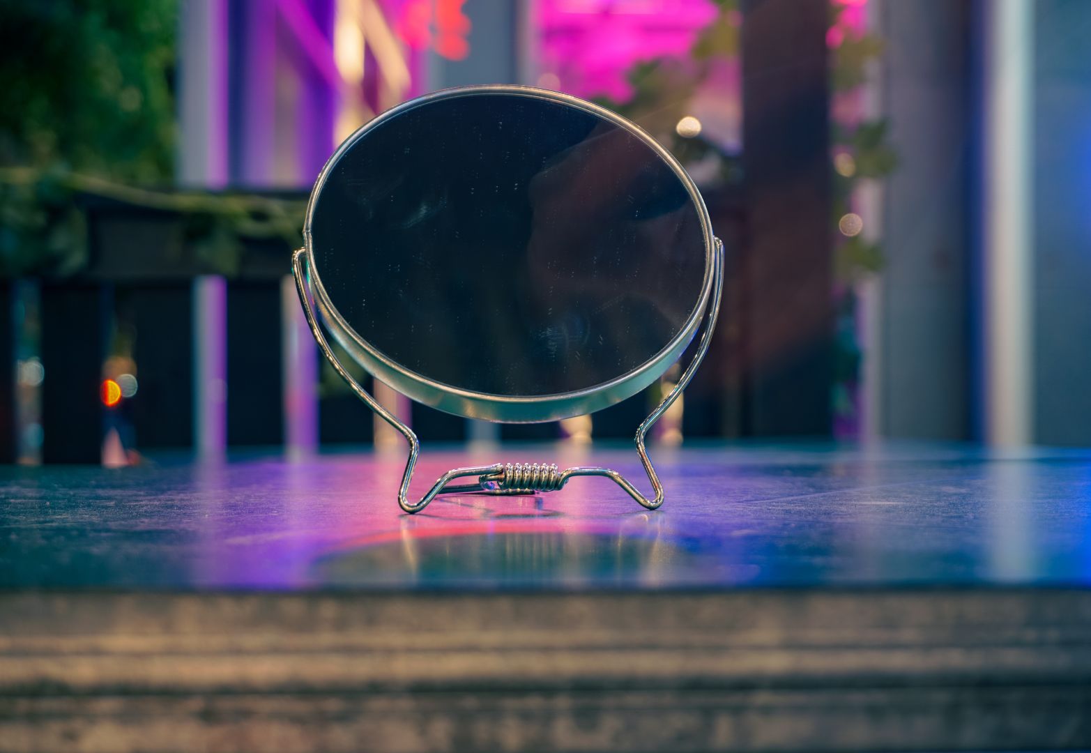 A mirror standing on metal surface with neon light in the background