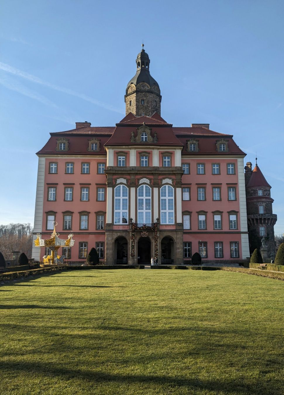 a façade of a castle painted pink, with three narrow arches for the main entrance, and a pristine lawn in front.