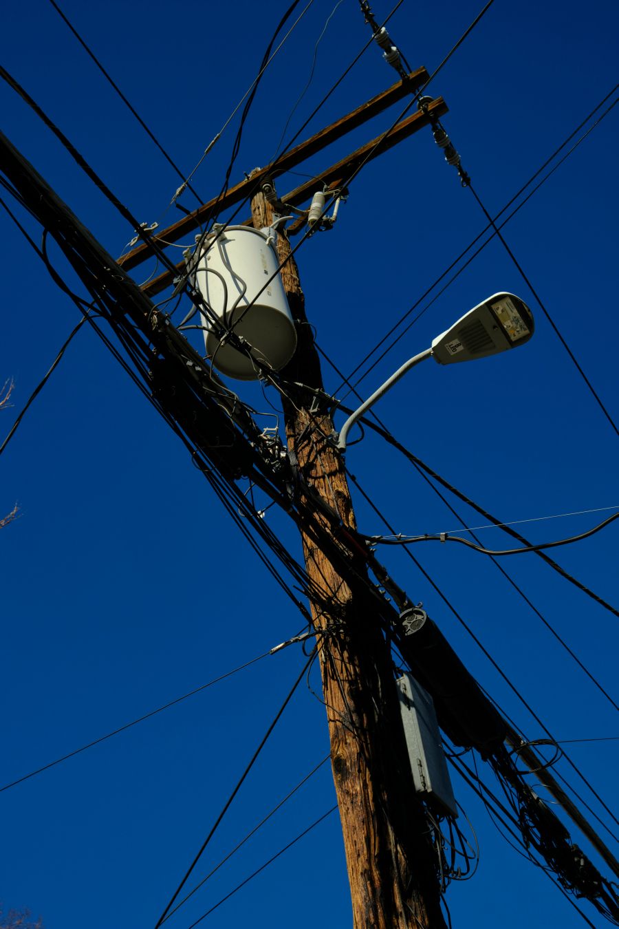 A photograph looking upwards at a battered electrical pole criss-crossed with a bewildering set of wires with a clear blue sky for a background.