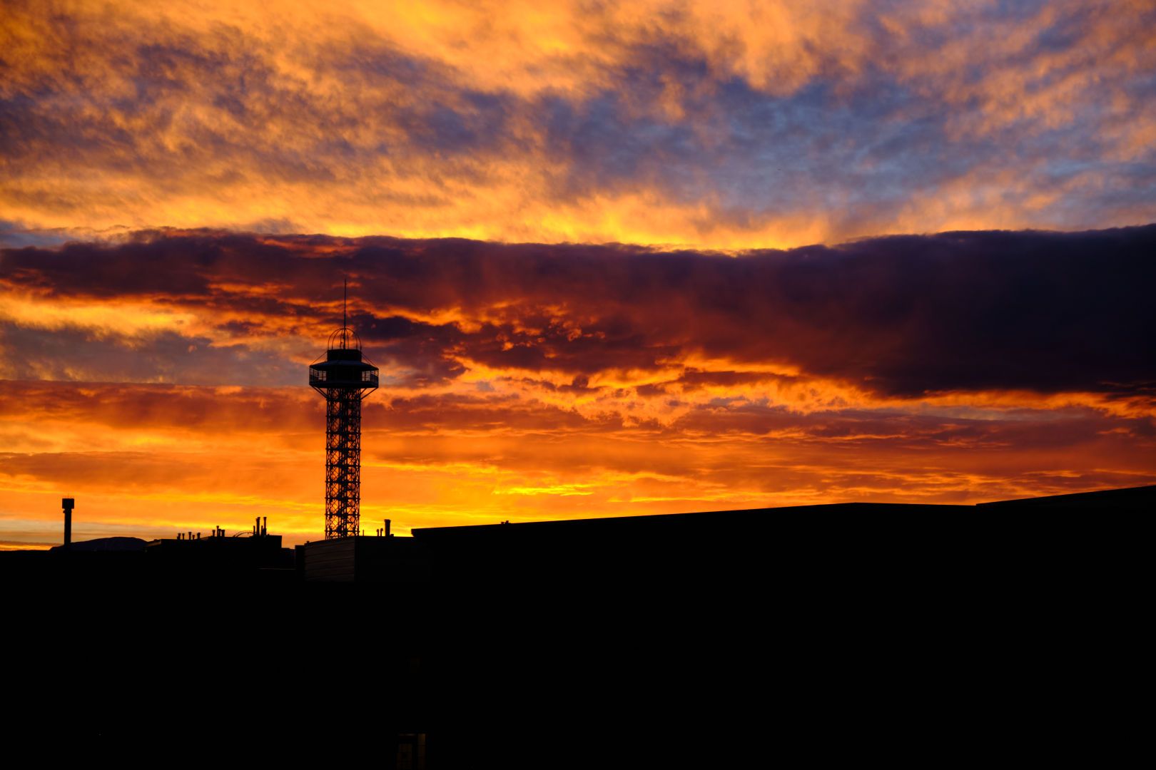 A photograph of a sunset with a silhouetted tower of an amusement park ride.