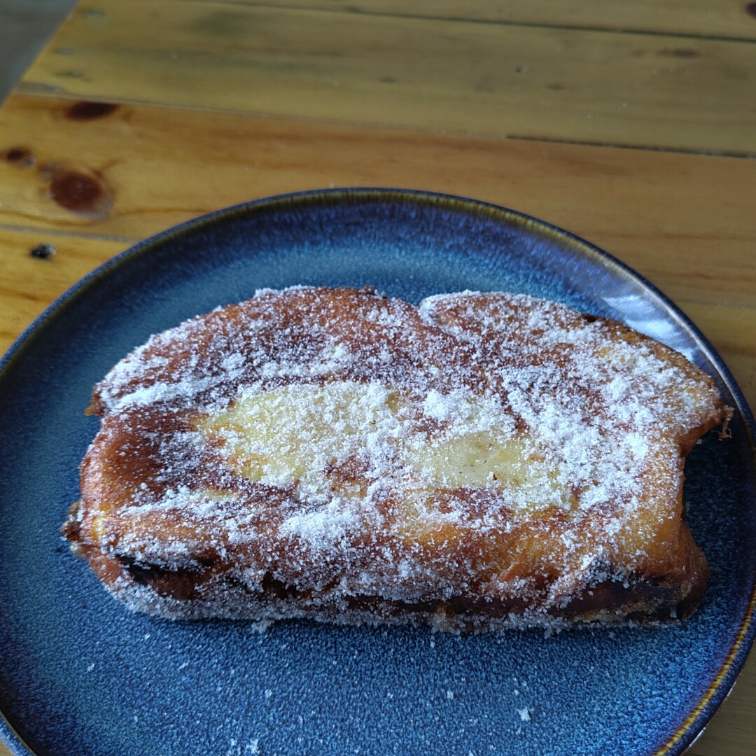 A "torrija" sprinkled with sugar and cinnamon, served on a blue ceramic plate that tests on a wooden table.