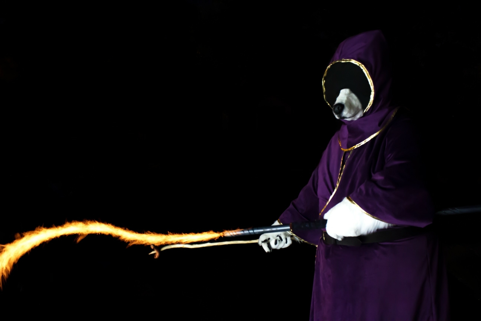 A white wolf wearing a purple hooded mage robe that hides his face. He is holding a sausage on a stick in one hand Yeah and a staff in the other, which he is using to cast a fire spell to cook the sausage.