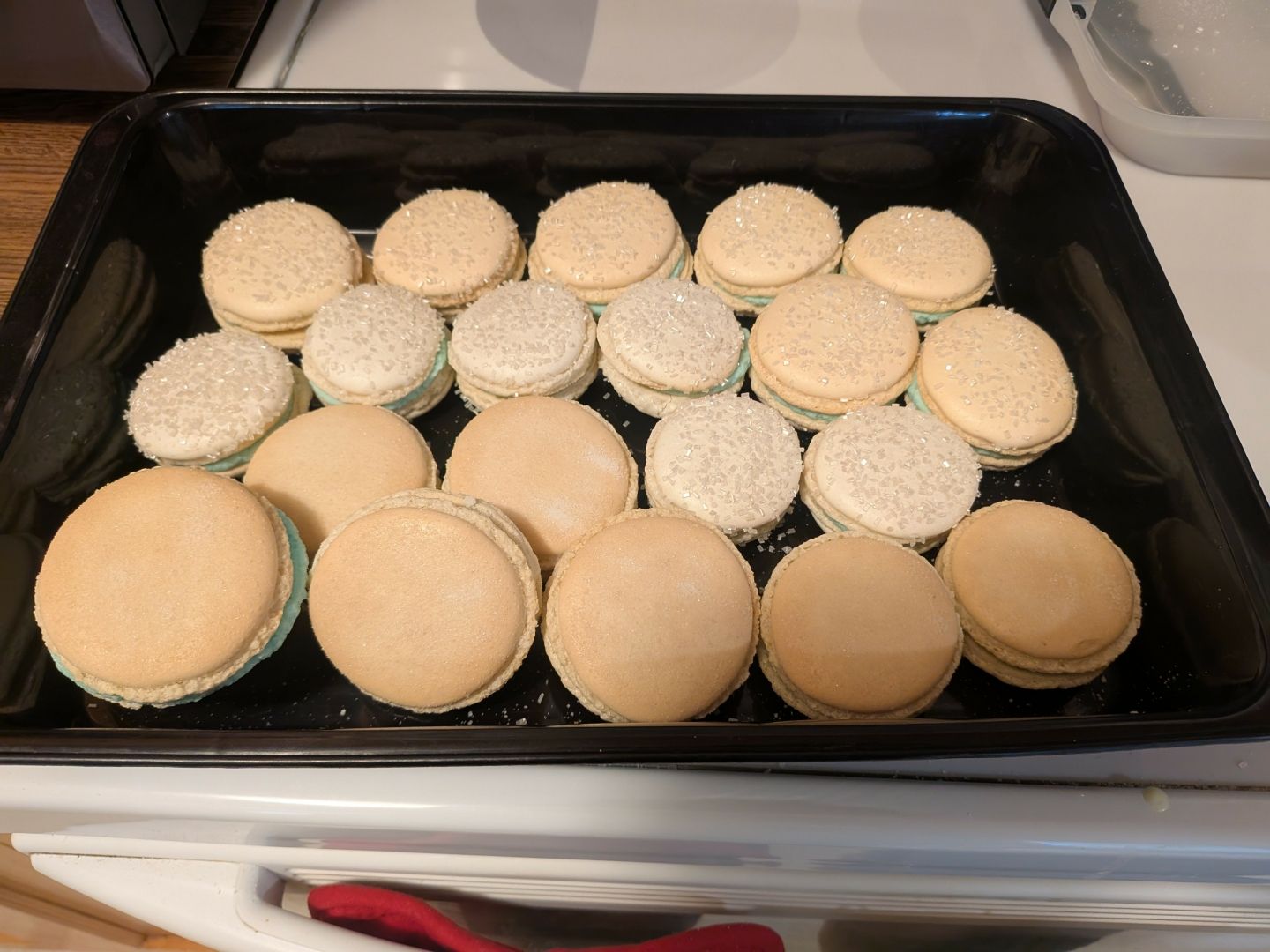 A black plastic tray holding 21 light tan macarons with a light blue ganache filling