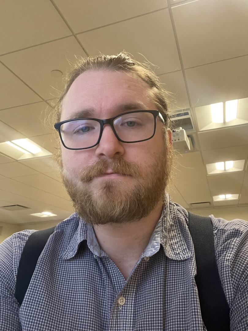 Sleepy bearded guy in glasses looking at the camera.