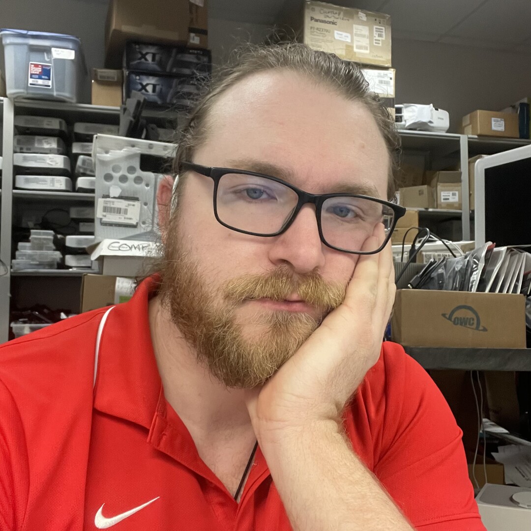 Bearded man in glasses, his cheek resting in his hand. He looks tired.