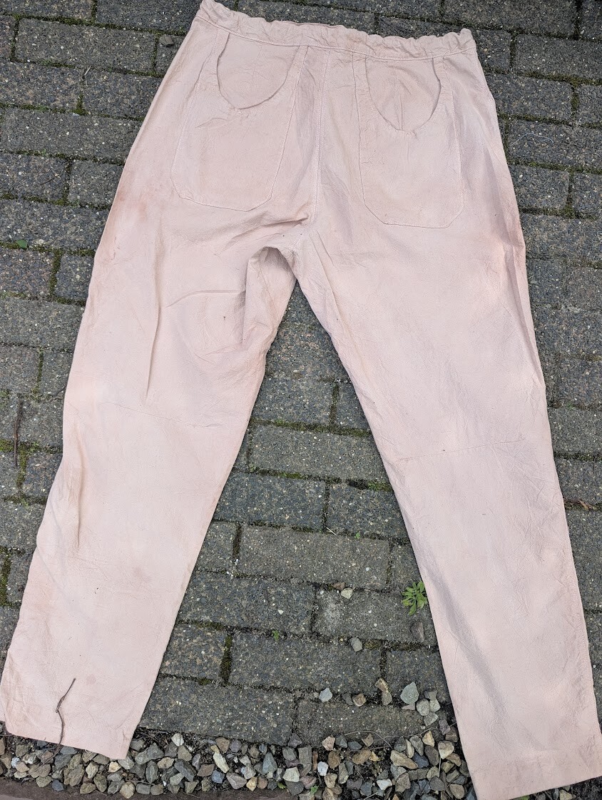 Full back view of a pair of handmade tan cotton pants, showing large patch pockets and an elasticated waistband, laid flat on brick pavers.