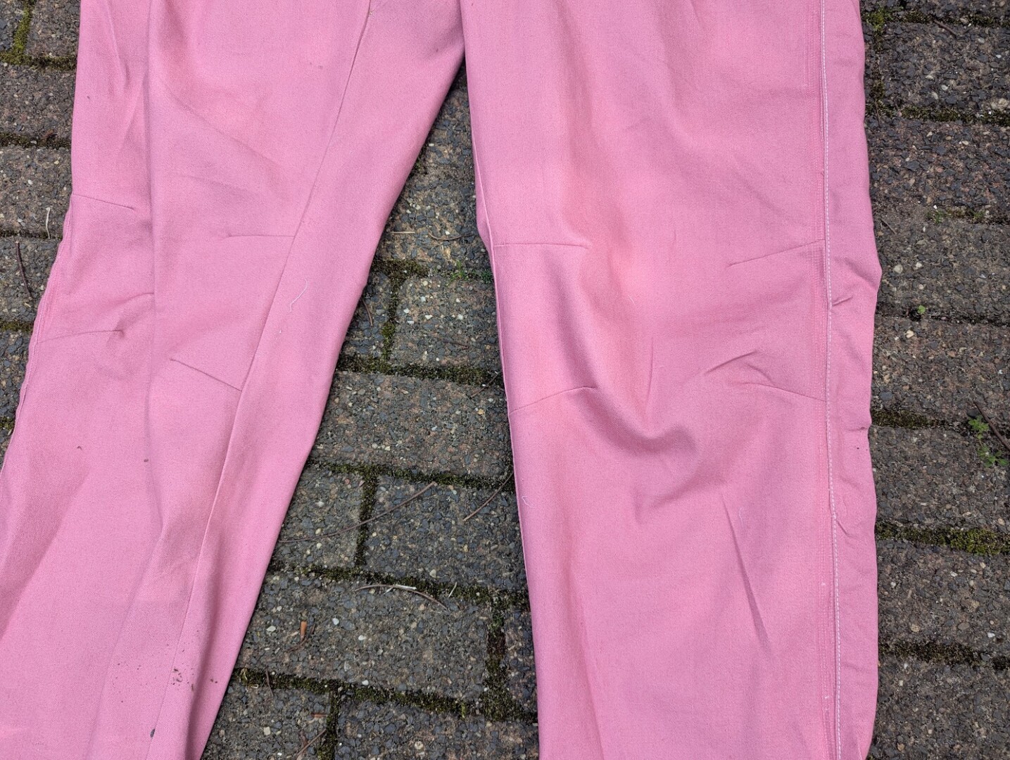 Close-up view of the articulated knee darts on the front legs of a pair of dusty pink denim pants.