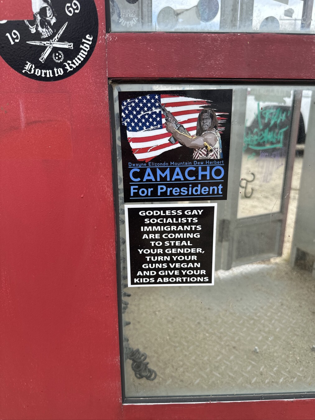 Close up of two stickers from the phone booth:

Dwayne Elizondo Mountain Dew Herbert
CAMACHO
For President

…and…

GODLESS GAY SOCIALISTS IMMIGRANTS ARE COMING TO STEAL
YOUR GENDER, TURN YOUR GUNS VEGAN AND GIVE YOUR KIDS ABORTIONS