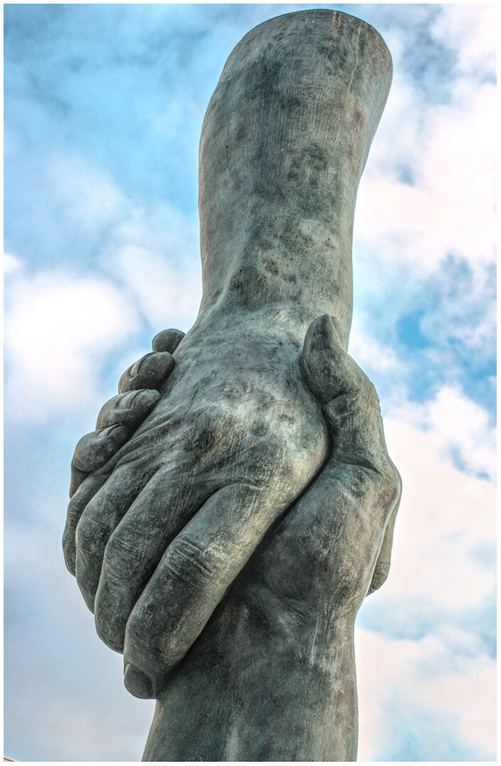 Escultura dunhas mans entrelazadas sobre un fondo de ceo azul con alguhna nube. (galego)

Sculpture of intertwined hands on a background of blue sky with a few clouds.