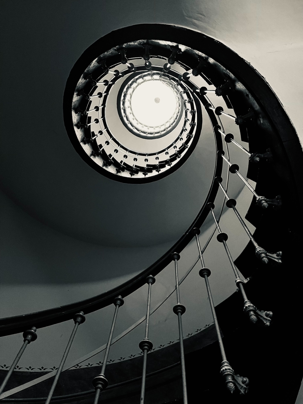 Black and white picture of a spiral staircase from the Bottom looking up to the round window in the ceiling with bright light