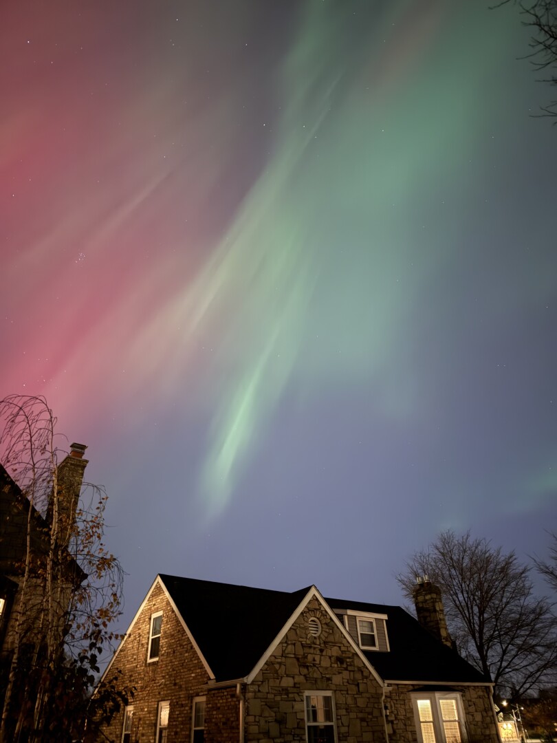 Photo of red and green streaky northern lights above a residential street