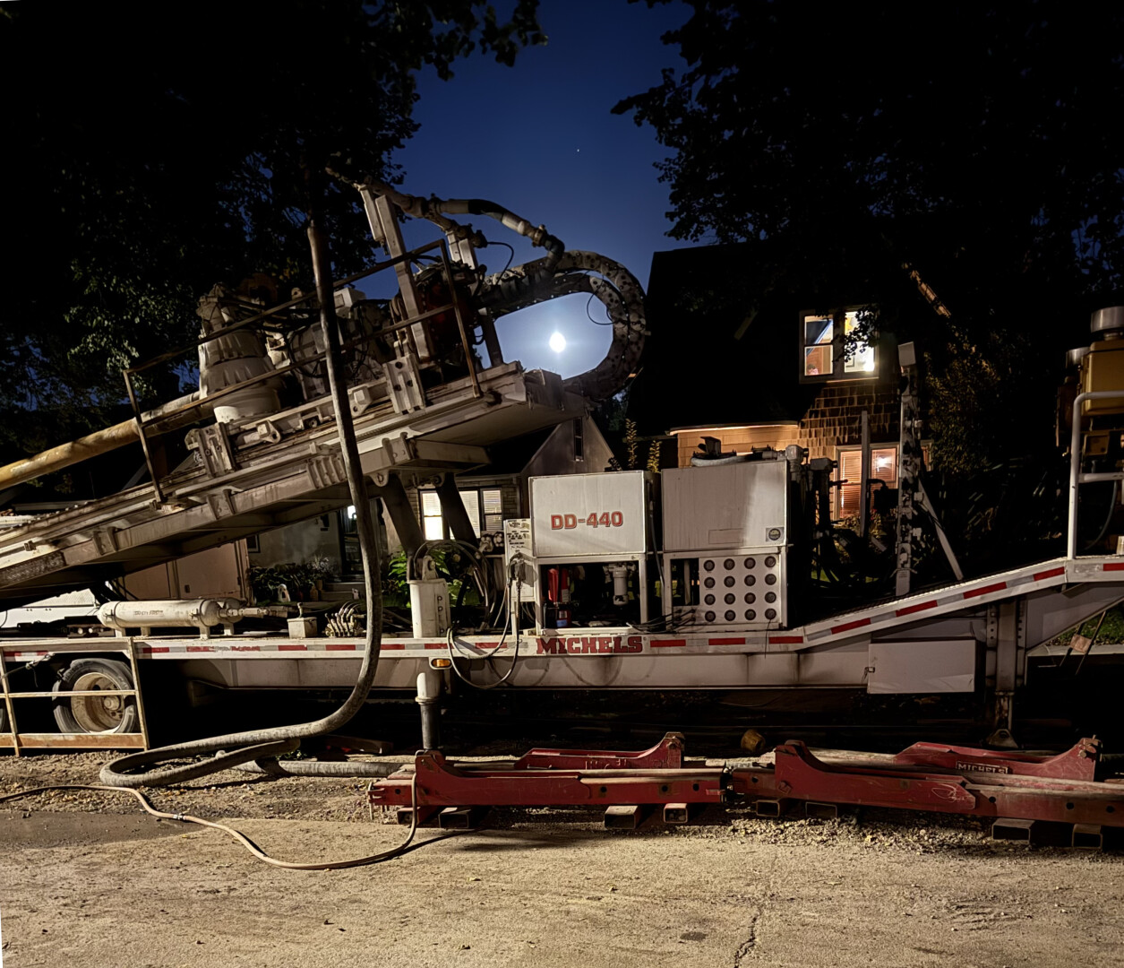 photo of a construction machine on a residential street at night, with the moon shining through a curve-edged opening