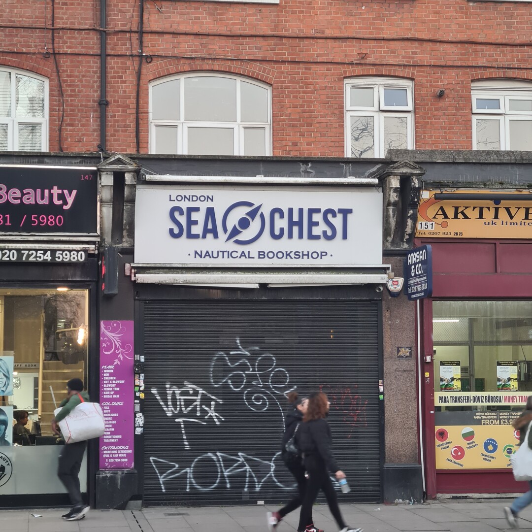 shop front with the sign: London Sea Chest Nautical Bookshop. shutters are down and have graffiti tags on