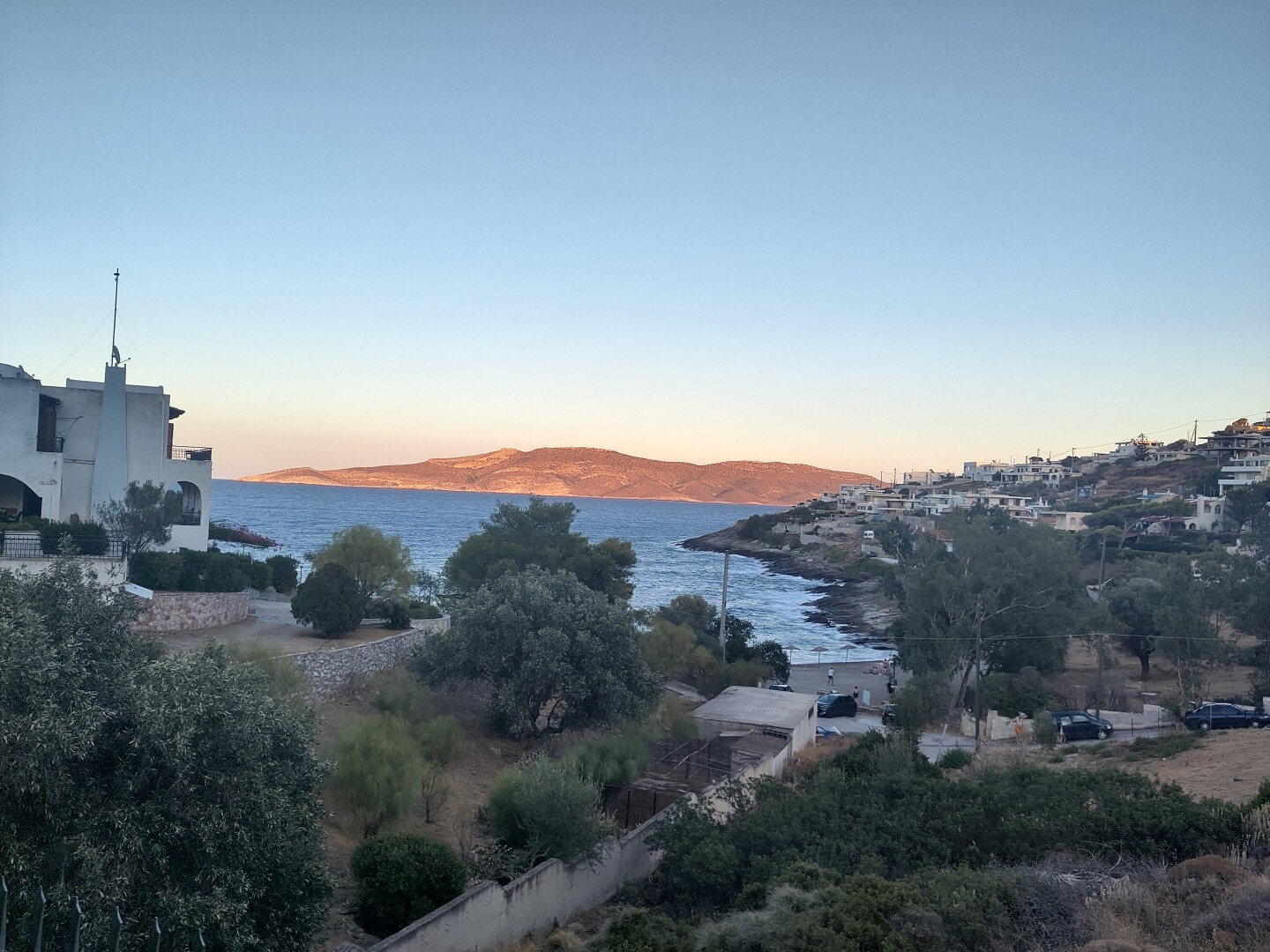 Our view at Keratea from the last apartment we stayed at, with one street leading down between greenery towards a small beach, clear blue waters stretching to the mountain range on the horizon.