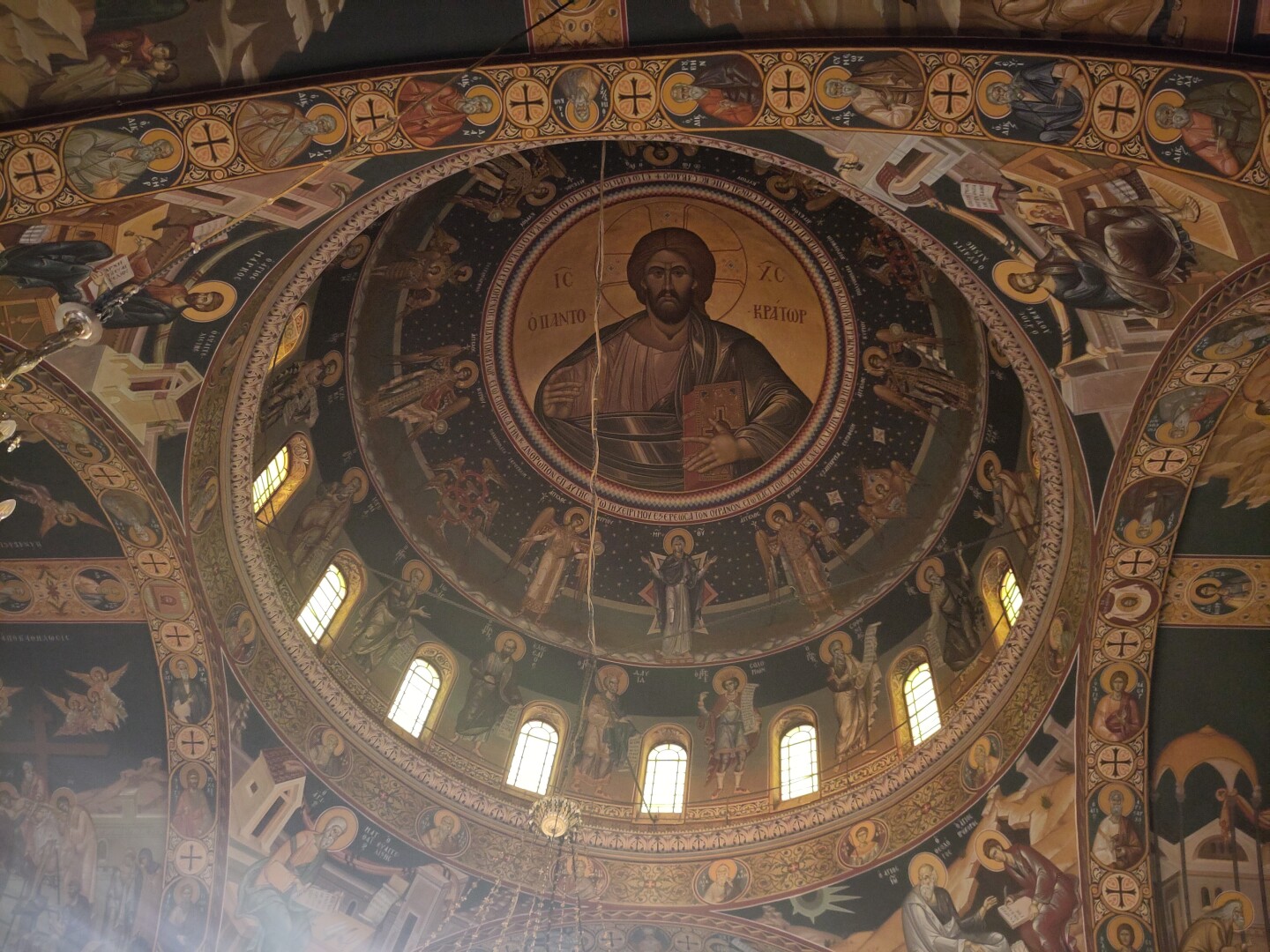 Upwards view of the church main dome interior, richly decorated in frescoes of a giant Jesus against a gold background in the middle of the dome, surrounded by a TON of saints (probably?) running along not just the inside of the dome, but also all the walls and beams. Light comes in from a row of arched windows along the bottom rim of the dome.
