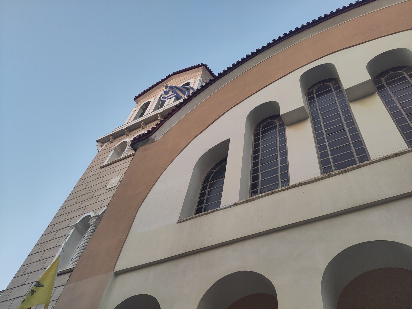An upwards angled shot of the front of the church, showing the tower at an angle on the left, overtaken towards the right by the arched curve that is the top of the main building, with a few narrow tall windows running along its width.