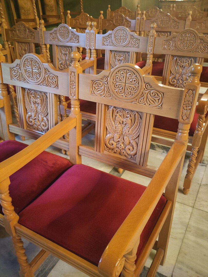 Close-up of the rows of wooden chairs in the church with their sturdy square shapes and intricate wood carvings on their backs, each chair accented by a red velvet pillow to sit on.