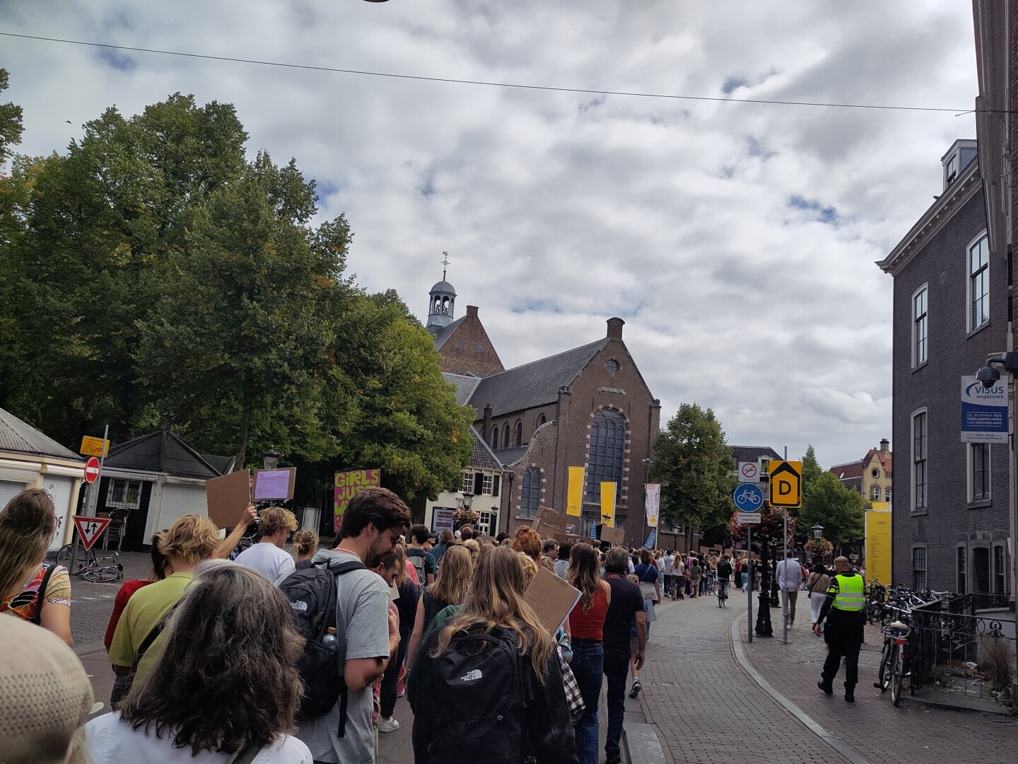 A wider street in front of St. Janskerk curving around a bend to the right, absolutely stuffed full of people protesting.
