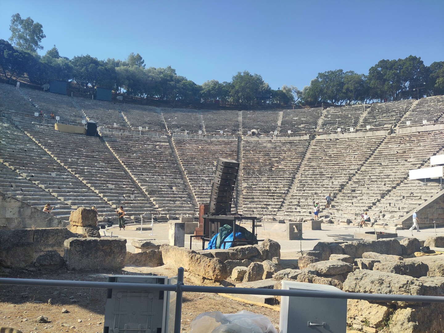 The main theater in Epidaurus, very large building of rows upon rows of seating space leading outwards and up into a typical half circle, framed by an outer treeline at the top. At the bottom is the stage, where performers can be heard from even without any modern amplification: the theater's natural acoustics amplify audio enough all on their own. You can even try it when visiting, it's great!