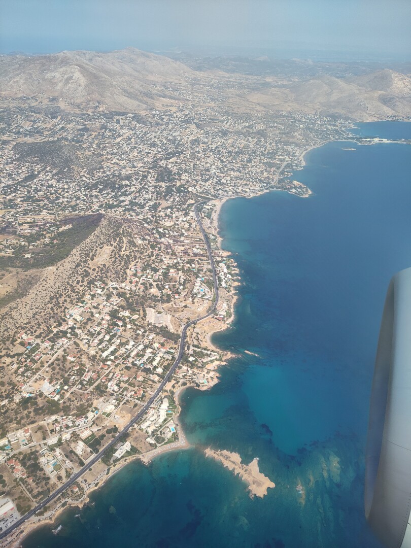 View from the airplane, showing a city along a coastline of beautiful clear blue waters, the Aegean Sea.