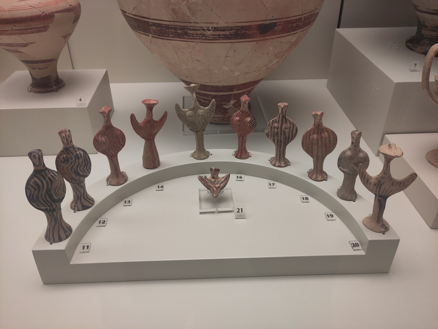 An assortment of very simply stylized little terracotta figurines - arranged and numbered in a semicircle. Some have their arms held upwards: so-called "psi" figurines, named after the Greek letter ψ. Others have arms down their sides resting on hips, their torsos forming a circle: so-called "phi" (θ) figurines.