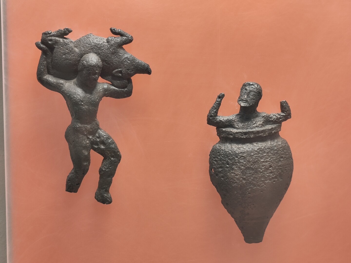 Close-up of a couple bronze-cast figurines from the Delphi Museum. To the left is Herakles carrying the Erymanthian boar across his shoulders. To the right is Eurystheus, the king of Argos, hiding in fear inside a jar.