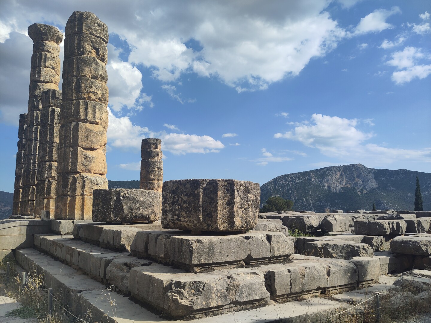 The Temple of Apollo with its remaining row of columns to the left, the rest of the temple base stretching to the right of the photo, with a mountain in the far background.
