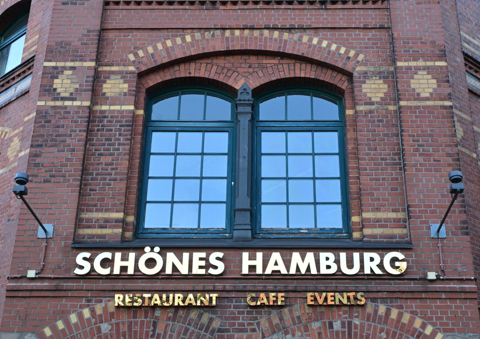 A brick building features two large arched windows and a sign that reads "SCHÖNES HAMBURG".