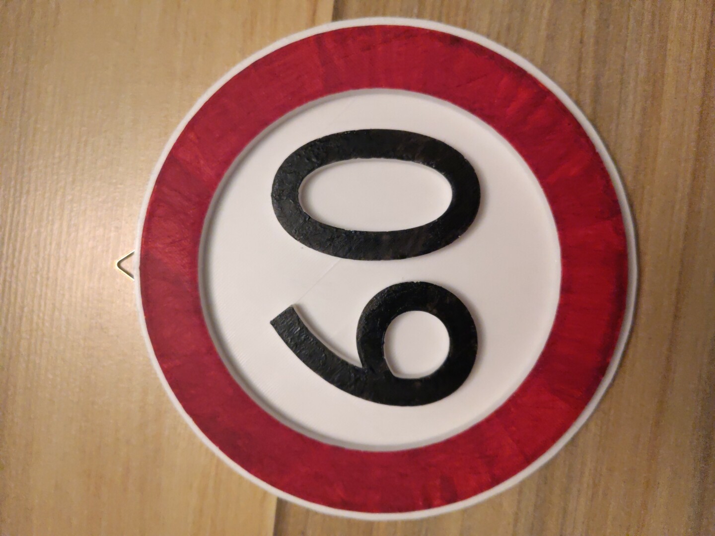 German Speed Limit sign for the speed limit 60 km/h, printed with a 3D Printer and manually painted. At the top, a hook has been added in order to be able to hang it onto the wall